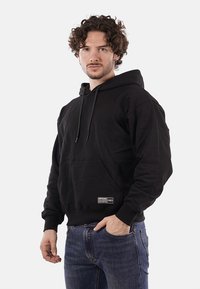 Felpa nera con cappuccio realizzata in misto cotone, dotata di tasca frontale, stringhe e un piccolo patch con logo sull'orlo inferiore.