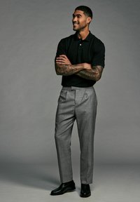 Sort polo skjorte, grå plisserede dressbukser og sorte lædersko. Stoffet har en subtil tekstur og en skræddersyet pasform.