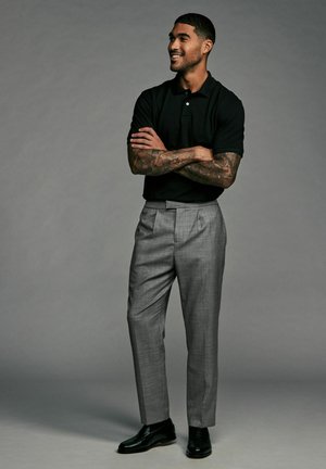 Sort polo skjorte, grå plisserede dressbukser og sorte lædersko. Stoffet har en subtil tekstur og en skræddersyet pasform.