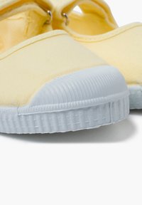 Scarpa da tela gialla con punta arrotondata, tomaia testurizzata e suola in gomma bianca con righe orizzontali e bordo liscio.