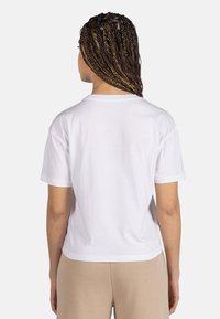 Camiseta de algodón blanca con mangas cortas, escote redondo, corte relajado y una textura suave, vista desde la parte de atrás.