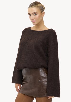 Pull en mohair marron avec une coupe ample, des manches larges et un col rond, associé à une minijupe en cuir marron, texture lisse.
