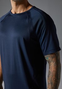 Marineblaues Sport-T-Shirt aus glattem Stoff, mit Rundhalsausschnitt und Raglanärmeln. Zeigt strukturierte Nahtdetails und eine körpernahe Passform.