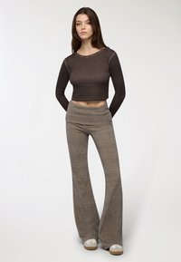 Brązowy krótki top z długim rękawem i okrągłym dekoltem w połączeniu z szarymi spodniami dzwonami. Oba elementy mają gładką teksturę i luźny krój.
