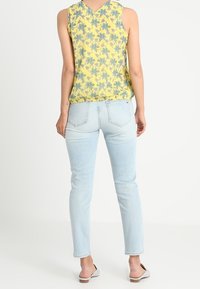 Gul blommig linne med v-ringning, kombinerat med ljusblå smala jeans. Tyget på linnet har en mjuk textur och ett mönstrat design.