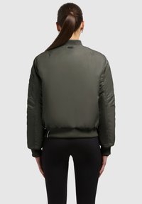 Olijfgroene bomberjack met een geribde kraag, elastische manchetten en een elastische boord. Kenmerken zijn onder andere stikselaccenten en een zijzak.