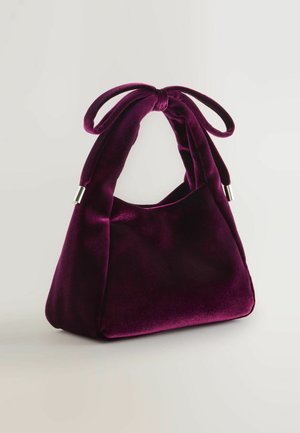 Paarse fluwelen handtas met een zachte textuur, een unieke vorm en een strikaccent aan de handgreep. Hardware in zilverkleur aan de basis.