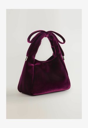 Purple velvet handbag with a soft texture, a unique shape, and a tied bow accent on the handle. Silver-tone hardware at the base.