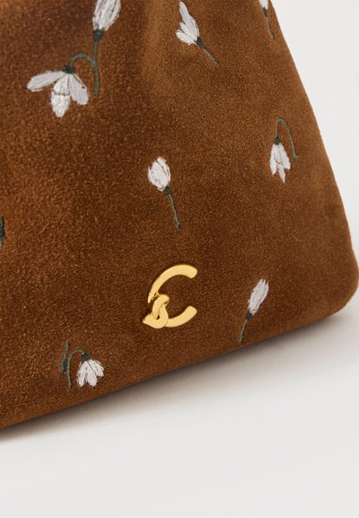Tissu en daim marron avec de petites fleurs blanches brodées et un logo C doré entrelacé sur la partie inférieure.