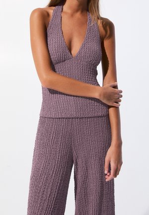 Woman wearing mauve textured sleeveless top with deep V-neck and matching wide-leg pants against white background.