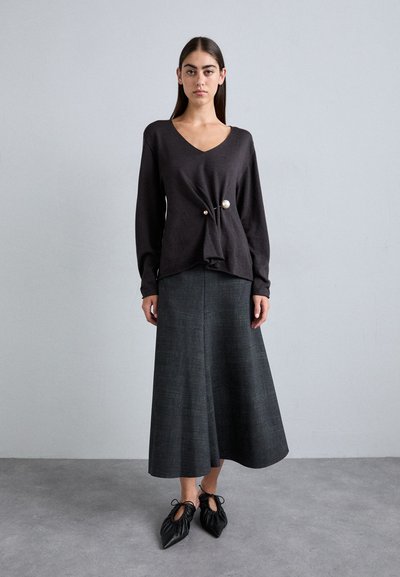 Dark gray long-sleeve top with a V-neck and knot detail, paired with a dark gray flared skirt and black pointed shoes with ties.