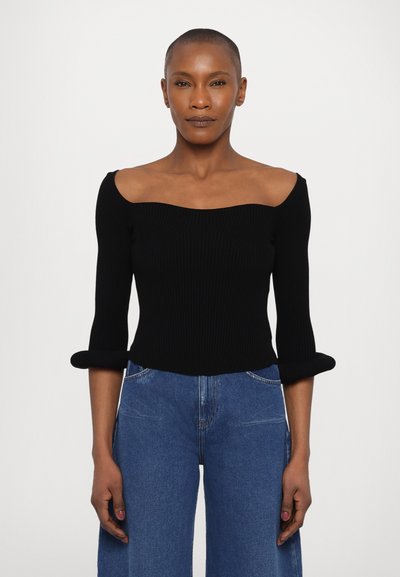 Haut en tricot noir côtelé avec un décolleté off-shoulder et des manches trois-quarts. Associé à un jean en denim bleu à jambes larges.