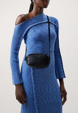 Czarna torba na ramię noszona na niebieskiej prążkowanej sukience z odkrytymi ramionami, z guzikami wzdłuż rękawa i bocznego szwu.