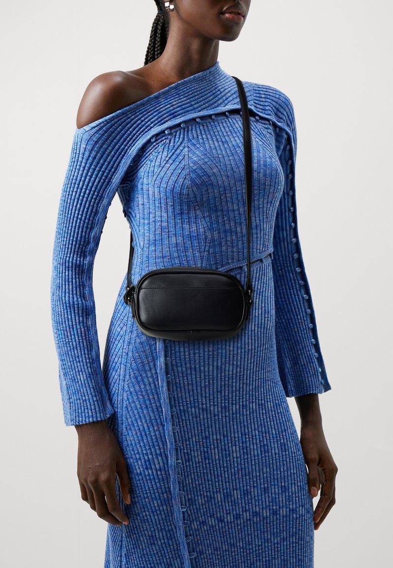 Czarna torba na ramię noszona na niebieskiej prążkowanej sukience z odkrytymi ramionami, z guzikami wzdłuż rękawa i bocznego szwu.