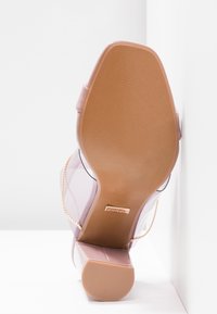 Chaussure à talon haut rose clair avec un dessus transparent, bout pointu et semelle beige. Présente un accent en chaîne en or rose.