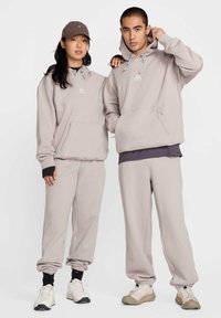 Sweatshirts gris clair et jogging assortis en tissu doux, dotés de poches kangourou, de poignets côtelés et d'accents de logo. Design décontracté.