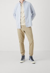 Gestreepte blauw-witte blouse, beige slim-fit broek en high-top sneakers in grijs en marineblauw met een crèmekleurige zool. Minimalistisch ontwerp, geen patronen.