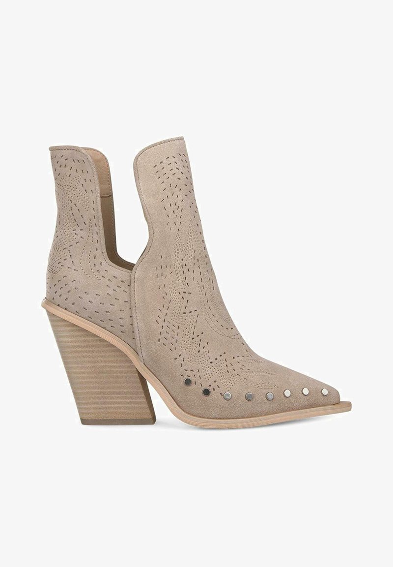 Stivale alla caviglia in suede beige con design a ritaglio, punta appuntita e tacco medio impilato. Presenta dettagli perforati e borchie metalliche.