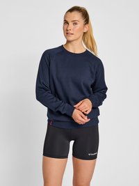 Sudadera azul marino con mangas raglán, material suave y puños acanalados. Combinada con pantalones cortos deportivos negros que tienen un logo en el dobladillo.