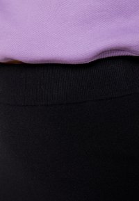 Lila Baumwoll-Sweatshirt, das über einem schwarzen elastischen Stoff getragen wird und sanfte Texturen sowie klare Kanten am Bund zeigt. Keine sichtbaren Muster.