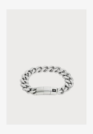Bracelet chaîne en métal argenté avec des maillons épais et un fermoir rectangulaire avec un petit logo noir.
