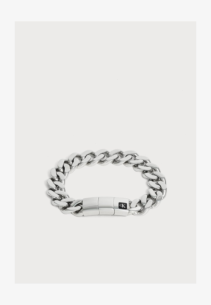 Bracelet chaîne en métal argenté avec des maillons épais et un fermoir rectangulaire avec un petit logo noir.