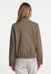 Veste courte olive, avec col, taille élastique et poignets à boutons. Le tissu est lisse avec des détails de coutures visibles.