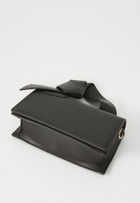 Bolso de piel sintética negra con una forma rectangular estructurada, que presenta un cierre con solapa plegada y una correa desmontable.