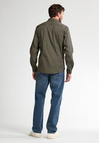 Gekleurde geruite shirt in groen en zwart, met een kraag en knoopmanchetten, gedragen met blauwe spijkerbroeken en witte sneakers, gezien van achteren.