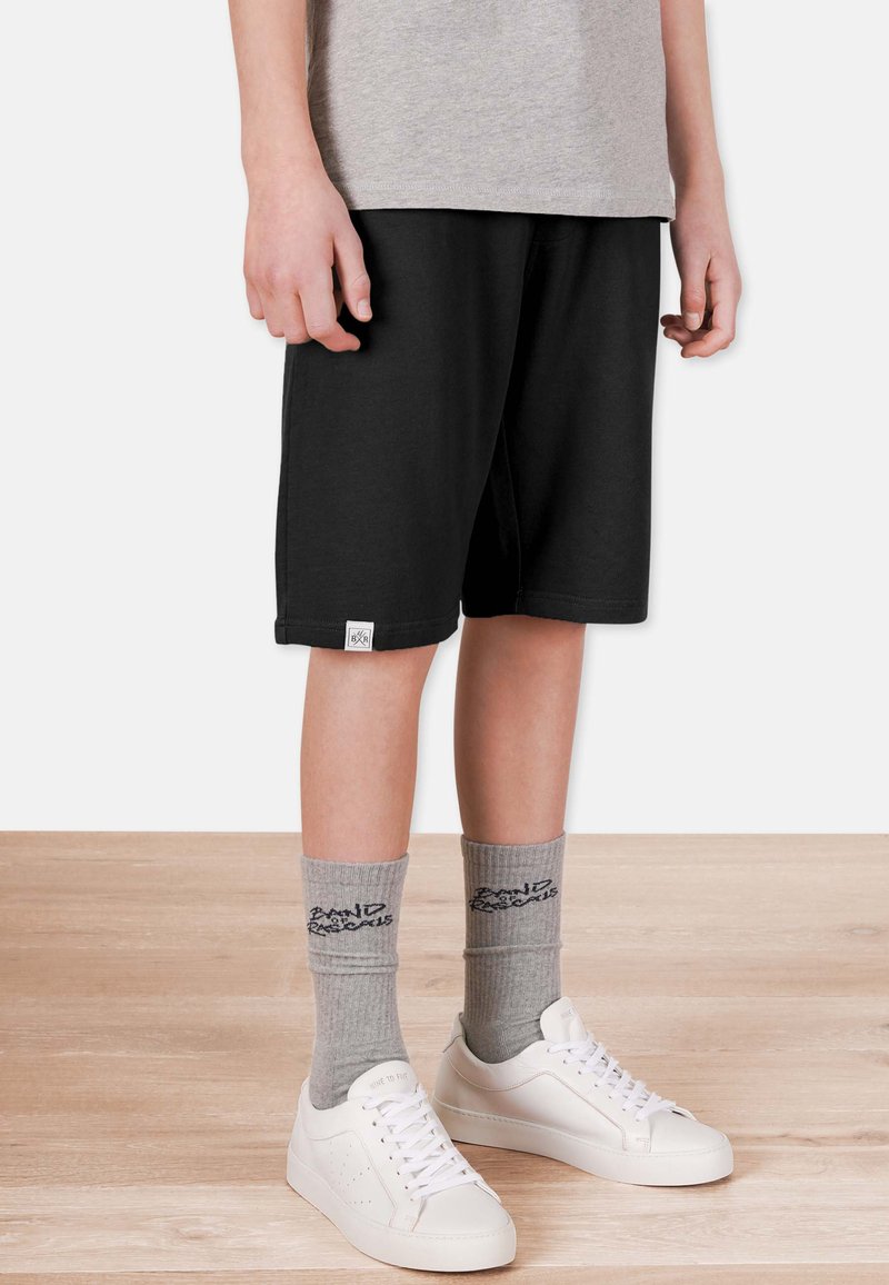 Svarta bomullsshorts med elastisk midja och en liten logotyp. I kombination med gråa strumpor och vita sneakers. Slät textur.