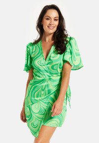 Green wrap dress with fluid swirl pattern, short puff sleeves, and tie detail at the waist. Made of lightweight, smooth fabric.
