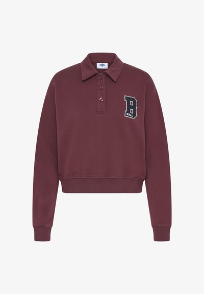 Burgundy színű, rövidített pólópulóver gallérral, három gombos gombolással és kontrasztos hímzett "B BALL" logóval a mellrészen. Puha textúra.