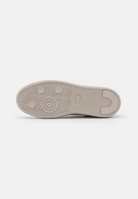 Sole di sneaker beige chiaro con motivo a spina di pesce, tacco arrotondato e dettagli di trazione circolari. Materiale in gomma e texture liscia.