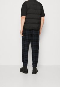 Svart vadderad väst över en svart t-shirt, tillsammans med marinblå rutiga byxor och svarta stövlar. Enfärgad textur, rutmönster på byxorna.