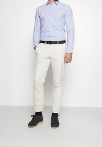 Hellblau gestreiftes Langarmhemd, cremfarbene Chinos und dunkle Schuhe mit heller Sohle, ergänzt durch einen schwarzen Gürtel. Einfaches und sauberes Design.
