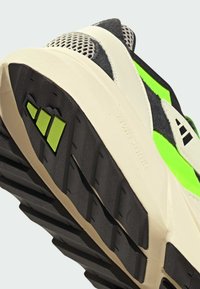 Buty sportowe z teksturowaną gumową podeszwą, z białymi, czarnymi i neonowo-zielonymi akcentami. Materiały obejmują siateczkę i zamsz.