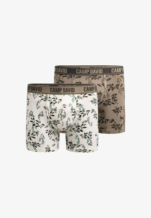 Muscular man with short brown hair wearing white boxer briefs with black leaf patterns and a beige waistband labeled "CAMP DAVID."
