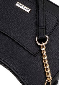 Pochette en cuir noir texturé avec un accent en chaîne dorée, dotée d'une poche rectangulaire à rabat et d'une plaque de marque. Fermeture éclair en bas.