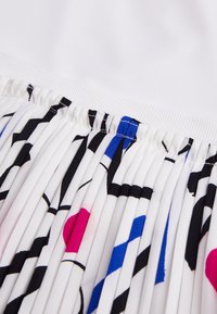 Sukně s plisováním, která má bílý spodní lem a barevné abstraktní vzory v růžové, modré a černé na bílém pozadí. Hladká textura.