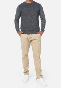 Szary sweter z dzianiny z prążkowanymi detalami, połączony z jasnobeżowymi chinosami i białymi tenisówkami. Prosty design i luźny krój.