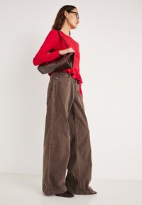 Brune vide bukser i teksturert stoff, kombinert med en rød langermet topp med rysjekant og en brun håndveske.