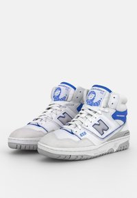Paire de baskets montantes New Balance 650 blanches et bleues avec lacets et semelles en caoutchouc, légèrement inclinées vers la droite.