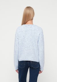 Jasnoniebieski sweter z dzianiny o luźnym kroju, długich rękawach i szerokim dekolcie. Miękka faktura i lekko skrócony krój. Połączony z ciemnymi dżinsami.