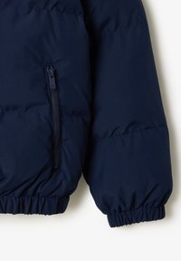 Section de doudoune bleu marine avec une poche latérale zippée. Caractéristiques : poignets froncés et texture lisse et brillante.