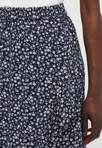 Jupe marine avec un petit motif floral blanc, taille élastique et texture douce. La vue en gros plan met en évidence les détails du tissu et du design.