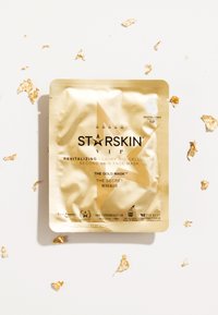 Emballage de masque facial en feuille d'or avec un design géométrique, comportant un texte noir et des accents de feuille d'or éparpillés sur un fond blanc.