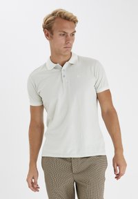 Svetlošedé polo tričko vyrobené z m�äkkej látky, s trojitou gombíkovou légiou, krátkymi rukávmi a diskrétnym logom na ľavej strane hrudníka.