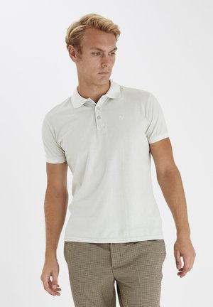 Heledhall hall polo särk, mis on valmistatud pehmest kangast, millel on kolme nupu rivi, lühikesed varrukad ja diskreetne logo vasakul rinnal.
