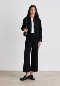 Black cropped jacket with button detail, white t-shirt, black wide-leg trousers, and black loafers, all placed against a neutral background.