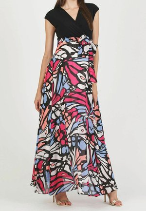 Femme portant un haut noir sans manches et une longue jupe colorée, brillante, à motif abstrait avec une ceinture nouée à la taille.